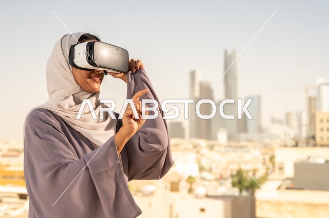 تقنيات حديثة الكترونية وأجهزة تكنولوجية، التفاعل ومحاكاة العالم الافتراضي الخيالي, صورة مقربة من الجانب لامرأة عربية خليجية سعودية محجبة تقف في المعرض تضع نظارات الفي ار, الاستمتاع في قضاء اوقات ترفيهية، قضاء وقت ممتع خارج المنزل