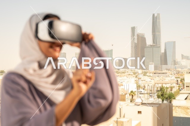 تقنيات حديثة الكترونية وأجهزة تكنولوجية، التفاعل ومحاكاة العالم الافتراضي الخيالي, صورة مقربة من الجانب لامرأة عربية خليجية سعودية محجبة تقف في المعرض تضع نظارات الفي ار, الاستمتاع في قضاء اوقات ترفيهية، قضاء وقت ممتع خارج المنزل