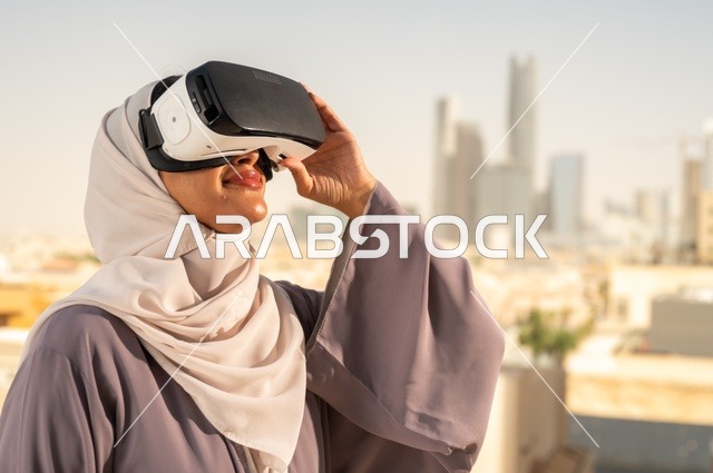 Modern electronic technologies and devices, interaction and simulation of the imaginary virtual world, a close-up side view of a Saudi Gulf Arab woman wearing a hijab standing in the exhibition wearing VR glasses, enjoying leisure time, having a good time outside the home.