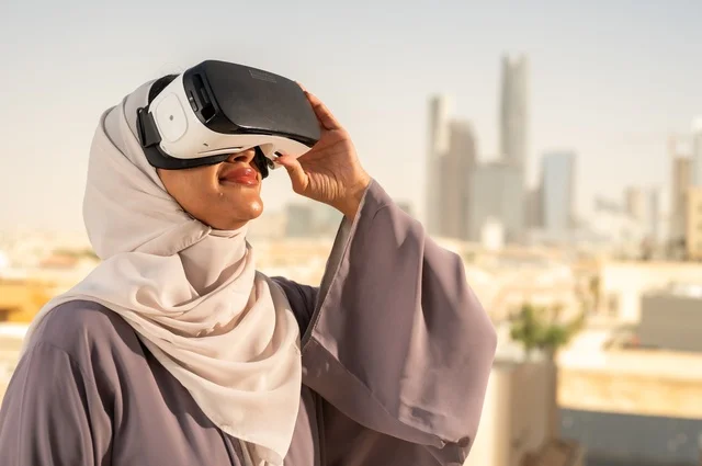 تقنيات حديثة الكترونية وأجهزة تكنولوجية، التفاعل ومحاكاة العالم الافتراضي الخيالي, صورة مقربة من الجانب لامرأة عربية خليجية سعودية محجبة تقف في المعرض تضع نظارات الفي ار, الاستمتاع في قضاء اوقات ترفيهية، قضاء وقت ممتع خارج المنزل