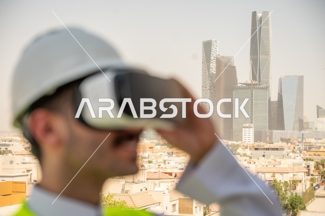  مفهوم أدارة المشاريع الهندسية، نمو وتطور الهندسة المعمارية على ايدي المبدعين أبناء الوطن، صورة جانبية مقربة لمهندس عربي خليجي سعودي يرتدي الثوب التقليدي والسترة الخاصة وخوذة الحماية ينظر في نظارة واقع افتراضي ثلاثية الأبعاد، خلفية أبراج وناطحات سحاب 