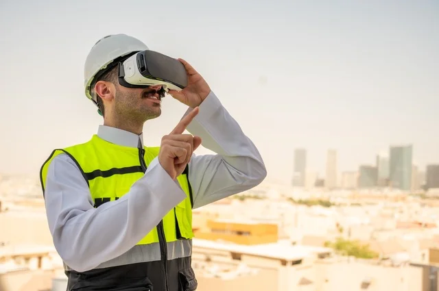  تقدم وتطور المباني في المملكة العربية السعودية، مفهوم أدارة المشاريع الهندسية، صورة جانبية لمهندس عربي خليجي سعودي يرتدي الثوب التقليدي والسترة الخاصة وخوذة الحماية ينظر في نظارة واقع افتراضي ثلاثية الأبعاد، خلفية أبراج وناطحات سحاب 