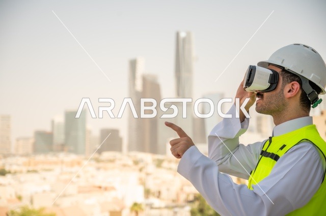  العمل في القطاع الهندسي، نمو وتطور الهندسة المعمارية على ايدي المبدعين أبناء الوطن، صورة جانبية لمهندس عربي خليجي سعودي يرتدي الثوب التقليدي والسترة الخاصة وخوذة الحماية ينظر في نظارة واقع افتراضي ثلاثية الأبعاد، خلفية أبراج وناطحات سحاب 