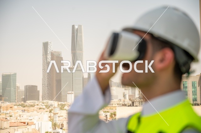  مفهوم أدارة المشاريع الهندسية، نمو وتطور الهندسة المعمارية على ايدي المبدعين أبناء الوطن، صورة جانبية مقربة لمهندس عربي خليجي سعودي يرتدي الثوب التقليدي والسترة الخاصة وخوذة الحماية ينظر في نظارة واقع افتراضي ثلاثية الأبعاد، خلفية أبراج وناطحات سحاب 