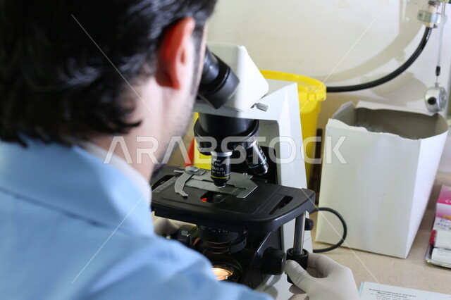 رجل عربي سعودي خليجي في المختبر  يفحص العينات عبر جهاز المجهر, مكبر العينات, تحاليل طبيه, مركز ابحاث عربي سعودي خليجي