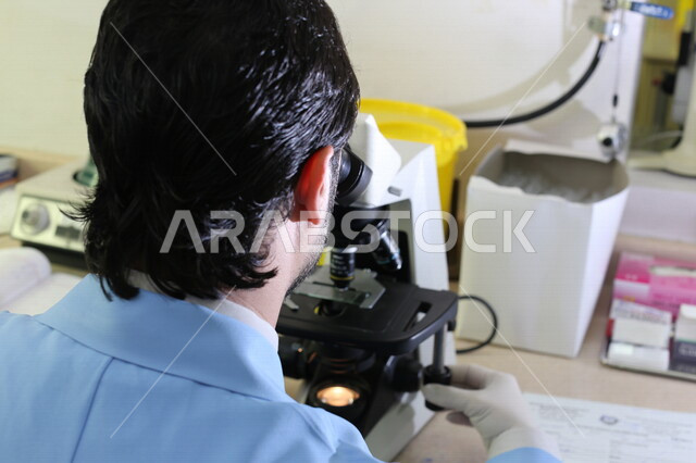 رجل عربي سعودي خليجي في المختبر  يفحص العينات عبر جهاز المجهر, مكبر العينات, تحاليل طبيه, مركز ابحاث عربي سعودي خليجي