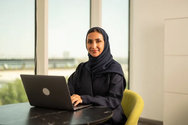 Remote business management, using a modern and advanced technical device, a Saudi Arabian Gulf woman wearing an abaya and hijab using a laptop in the office, integrating technology into work, completing required tasks via laptop, a female office profession and job