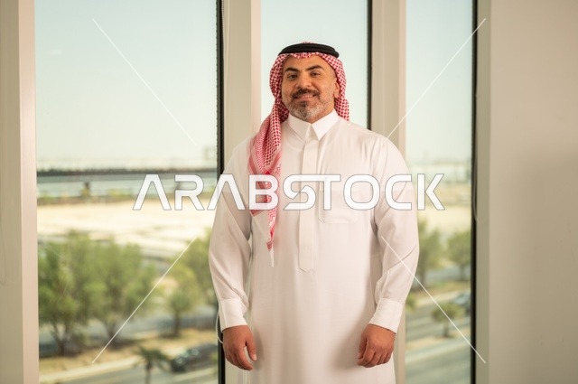 الفخر والاعتزاز بالدولة السعودية، أبراج وناطحات سحاب مدينة الرياض، رجل عربي خليجي سعودي يرتدي الثوب والشماغ التقليدي يقف باستقامة بايماءات السرور، التقدم والتطور المعماري في دول الخليج