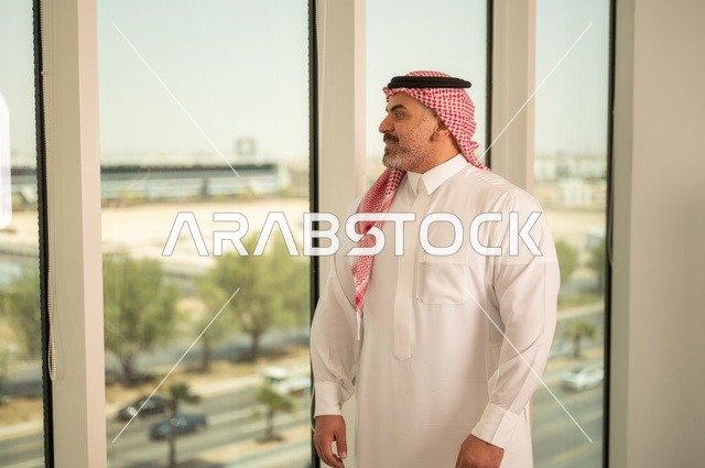 الفخر والاعتزاز بالدولة السعودية، أبراج وناطحات سحاب مدينة الرياض، رجل عربي خليجي سعودي يرتدي الثوب والشماغ التقليدي يقف باستقامة بايماءات السرور، التقدم والتطور المعماري في دول الخليج