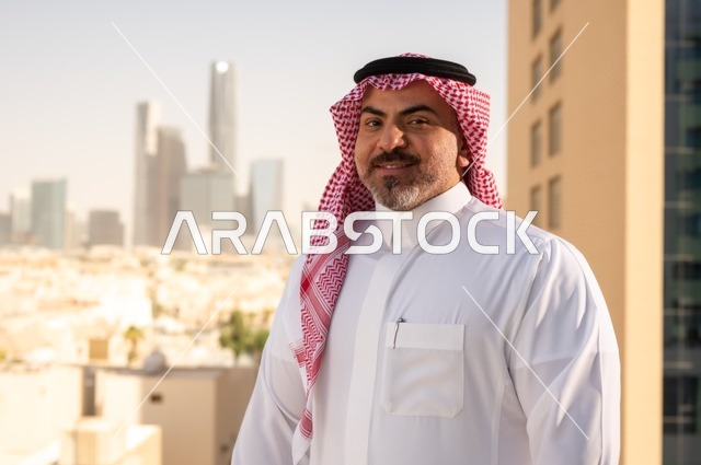 الفخر والاعتزاز بالدولة السعودية، أبراج وناطحات سحاب مدينة الرياض، رجل عربي خليجي سعودي يرتدي الثوب والشماغ التقليدي يقف باستقامة بايماءات السرور، التقدم والتطور المعماري في دول الخليج