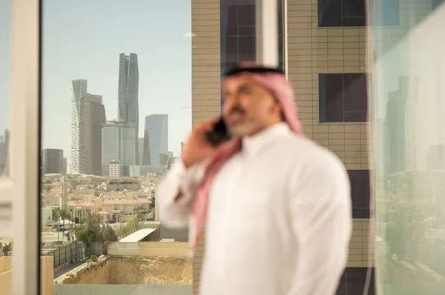 استخدام جهاز تقني حديث ومتطور،  رجل عربي خليجي سعودي يرتدي الثوب التقليدي يقوم بإجراء مكالمة هاتفية عبر الهاتف المحمول، التقدم والتطور المعماري في دول الخليج، خلفية الأبراج وناطحات السحاب في مدينة الرياض
