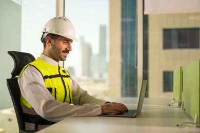 متابعة مخطط المشروع الهندسي اونلاين, مفهوم الهندسة المعمارية، مشاريع إعمارية سعودية وطنية، الاهتمام بالتطور العمراني بسواعد المهندسين السعوديين, مهندس عربي خليجي سعودي يرتدي سترة العمل وخوذة الحماية البيضاء ينجز المهام اليومية عبر الحاسب المحمول