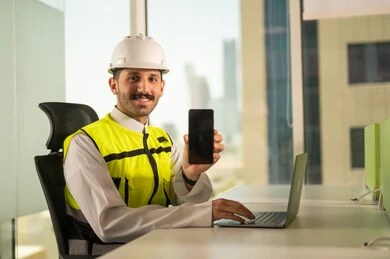 عرض شاشة هاتف محمول سوداء فارغة, متابعة مخطط المشروع الهندسي اونلاين,  مشاريع إعمارية سعودية وطنية، الاهتمام بالتطور العمراني بسواعد المهندسين السعوديين, مهندس عربي خليجي سعودي يرتدي سترة العمل وخوذة الحماية البيضاء ينجز المهام اليومية عبر الحاسب المحمول