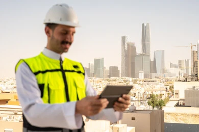 دمج التقنية في الهندسة المعمارية, متابعة مخطط المشروع الهندسي اونلاين, مشاريع إعمارية سعودية وطنية، الاهتمام بالتطور العمراني بسواعد المهندسين السعوديين, مهندس عربي خليجي سعودي يرتدي سترة العمل وخوذة الحماية البيضاء ينجز المهام اليومية عبر جهاز التابلت