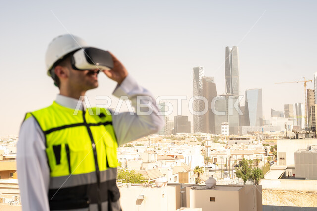 رؤية مخطط المشروع الهندسي عبر الفي الار, مشاريع إعمارية سعودية وطنية، الاهتمام بالتكنولوجيا والتطور العمراني, مهندس عربي خليجي سعودي يرتدي سترة العمل وخوذة الحماية البيضاء يقوم بدراسة المشروع باستخدام نظارة الواقع الافتراضي, دمج التقنية في الهندسة المعمارية