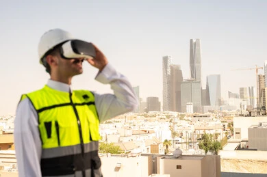 رؤية مخطط المشروع الهندسي عبر الفي الار, مشاريع إعمارية سعودية وطنية، الاهتمام بالتكنولوجيا والتطور العمراني, مهندس عربي خليجي سعودي يرتدي سترة العمل وخوذة الحماية البيضاء يقوم بدراسة المشروع باستخدام نظارة الواقع الافتراضي, دمج التقنية في الهندسة المعمارية