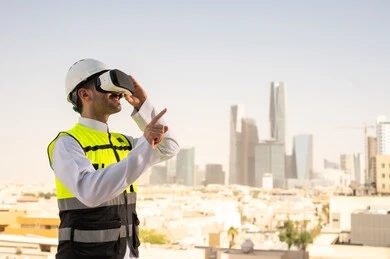 Viewing the engineering project plan via VR, Saudi national construction projects, interest in technology and urban development, a Saudi Gulf Arab engineer wearing a work jacket and white protective helmet studying the project using virtual reality glasses, integrating technology into architecture