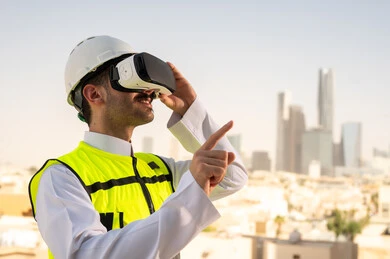 رؤية مخطط المشروع الهندسي عبر الفي الار, مشاريع إعمارية سعودية وطنية، الاهتمام بالتكنولوجيا والتطور العمراني, مهندس عربي خليجي سعودي يرتدي سترة العمل وخوذة الحماية البيضاء يقوم بدراسة المشروع باستخدام نظارة الواقع الافتراضي, دمج التقنية في الهندسة المعمارية