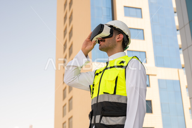 رؤية مخطط المشروع الهندسي عبر الفي الار, مشاريع إعمارية سعودية وطنية، الاهتمام بالتكنولوجيا والتطور العمراني, مهندس عربي خليجي سعودي يرتدي سترة العمل وخوذة الحماية البيضاء يقوم بدراسة المشروع باستخدام نظارة الواقع الافتراضي, دمج التقنية في الهندسة المعمارية