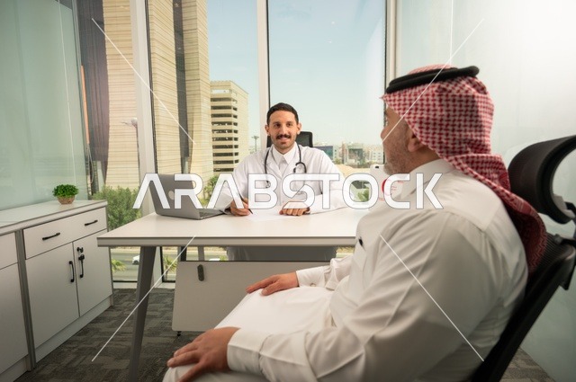 الحوار مع المرضى لكشف الحالة، تقديم الاستشارات في المراكز الطبيه, متابعة السجل الطبي للمراجعين, العمل في القطاعات الصحية, تسجيل حالات المرضى على جهاز الحاسوب, طبيب عربي خليجي سعودي يرتدي المعطف الأبيض يقوم بشرح الحالة المرضية لمريض يرتدي الشماغ والثوب التقليدي