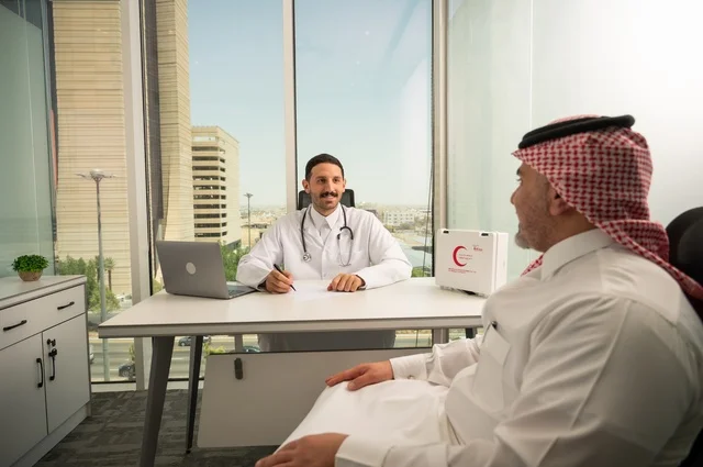 الحوار مع المرضى لكشف الحالة، تقديم الاستشارات في المراكز الطبيه, متابعة السجل الطبي للمراجعين, العمل في القطاعات الصحية, تسجيل حالات المرضى على جهاز الحاسوب, طبيب عربي خليجي سعودي يرتدي المعطف الأبيض يقوم بشرح الحالة المرضية لمريض يرتدي الشماغ والثوب التقليدي