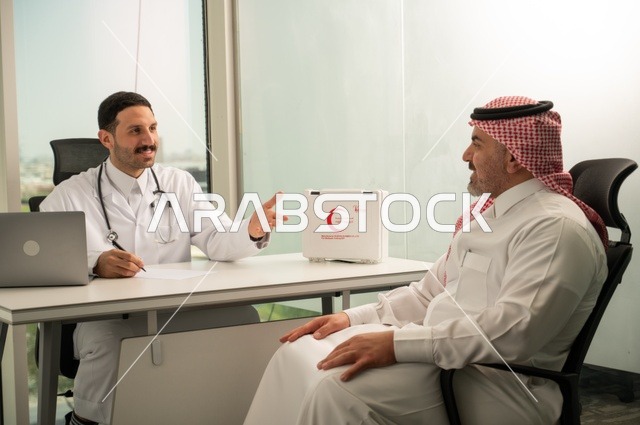الحوار مع المرضى لكشف الحالة، تقديم الاستشارات في المراكز الطبيه, متابعة السجل الطبي للمراجعين, العمل في القطاعات الصحية, تسجيل حالات المرضى على جهاز الحاسوب, طبيب عربي خليجي سعودي يرتدي المعطف الأبيض يقوم بشرح الحالة المرضية لمريض يرتدي الشماغ والثوب التقليدي