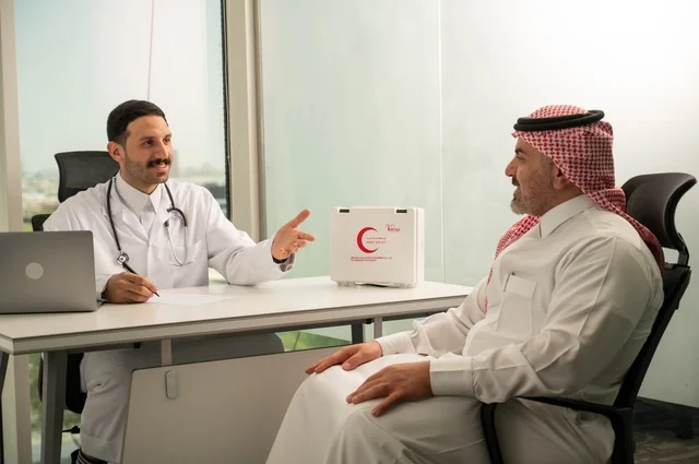 الحوار مع المرضى لكشف الحالة، تقديم الاستشارات في المراكز الطبيه, متابعة السجل الطبي للمراجعين, العمل في القطاعات الصحية, تسجيل حالات المرضى على جهاز الحاسوب, طبيب عربي خليجي سعودي يرتدي المعطف الأبيض يقوم بشرح الحالة المرضية لمريض يرتدي الشماغ والثوب التقليدي