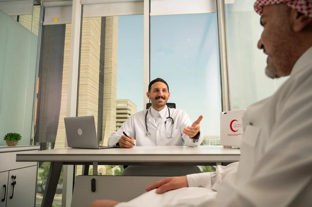 متابعة السجل الطبي للمراجعين, تسجيل حالات المرضى على جهاز الحاسوب, طبيب عربي خليجي سعودي يرتدي المعطف الأبيض يقوم بشرح الحالة المرضية لمريض يرتدي الشماغ والثوب التقليدي، الحوار مع المرضى لكشف الحالة، تقديم الاستشارات في المراكز الطبيه, العمل في القطاعات الصحية