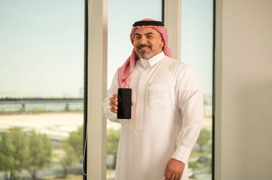 Blank black screen, modern and advanced technical device, Saudi Arabian Gulf man wearing traditional thobe and shemagh using mobile phone, doing remote work, background of towers and skyscrapers in Riyadh