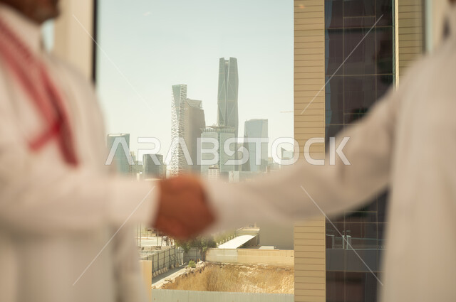 الشراكة في الأعمال والمشاريع الهندسية، صداقات وتعارف وبناء علاقات اجتماعية، عقد صفقات عمل جديدة ناجحة بين رجال الأعمال، صورة مقربة لايدي رجلين سعوديين عربيين خليجيين يرتديان الزي التقليدي يقومان بمصافحة بعضهما، توسيع مجالات العمل