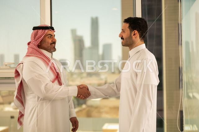  صداقات وتعارف وبناء علاقات اجتماعية، عقد صفقات عمل جديدة ناجحة بين رجال الأعمال، رجلان سعوديان عربيان خليجيان يرتديان الزي التقليدي يقومان بمصافحة بعضهما، توسيع مجالات العمل, الشراكة في الأعمال والمشاريع الهندسية