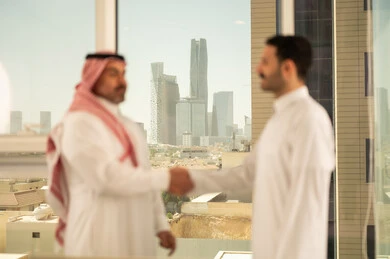 Friendships, acquaintances, and building social relationships, concluding new successful business deals between businessmen, two Saudi Arabian Gulf men wearing traditional dress shaking hands, expanding business areas, partnership in business and engineering projects