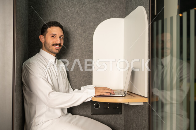 Business administration and organization, use of modern and advanced technical equipment, office administrative profession and job, a Saudi Arabian Gulf man wearing traditional thobe working on a laptop in the office, companies and offices in the Kingdom of Saudi Arabia
