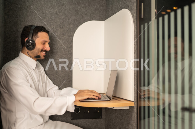 إدارة شؤون الأعمال وتنظيمها، استخدام جهاز تقني حديث ومتطور، مهنة ووظيفة ادارية مكتبية، رجل عربي خليجي سعودي يرتدي الثوب التقليدي يقوم بالعمل على الحاسوب المحمول داخل المكتب، الشركات والمكاتب في المملكة العربية السعودية