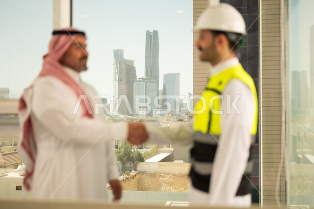 إيماءات المصافحة والترحيب والاستقبال, مفهوم التعاون والعمل المشترك, مهندس عربي خليجي سعودي يرتدي الخوذة وسترة الحماية يقوم بالتصافح مع رجل اعمال, الاتفاق على الخطط والمشاريع الهندسية في موقع العمل , الإنشاءات المعمارية في الأراضي السعودية