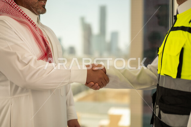 تعابير المصافحة والترحيب والاستقبال, مفهوم التعاون والعمل المشترك, صورة مقربة لايدي مهندس عربي خليجي سعودي يرتدي الخوذة وسترة الحماية يقوم بالتصافح مع رجل اعمال, الاتفاق على الخطط والمشاريع الهندسية في موقع العمل , الإنشاءات المعمارية في الأراضي السعودية