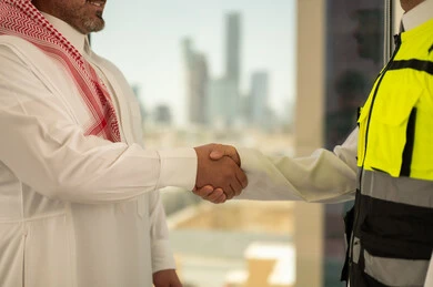 تعابير المصافحة والترحيب والاستقبال, مفهوم التعاون والعمل المشترك, صورة مقربة لايدي مهندس عربي خليجي سعودي يرتدي الخوذة وسترة الحماية يقوم بالتصافح مع رجل اعمال, الاتفاق على الخطط والمشاريع الهندسية في موقع العمل , الإنشاءات المعمارية في الأراضي السعودية