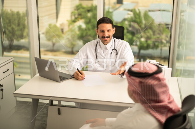  تسجيل حالات المرضى على جهاز الحاسوب, طبيب عربي خليجي سعودي يرتدي المعطف الأبيض يقوم بشرح الحالة المرضية لمريض يرتدي الشماغ والثوب التقليدي, الحوار مع المرضى لكشف الحالة، تقديم الاستشارات في المراكز الطبيه, متابعة السجل الطبي للمراجعين, العمل في القطاعات الصحية