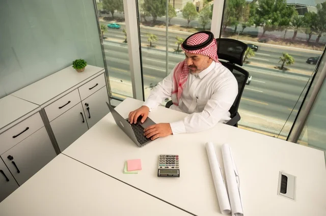 إدارة شؤون الأعمال وتنظيمها، استخدام جهاز تقني حديث ومتطور، مهنة ووظيفة ادارية مكتبية، موظف عربي خليجي سعودي يرتدي الثوب والشماغ التقليدي يقوم بالعمل على الحاسوب المحمول داخل المكتب، الشركات والمكاتب في المملكة العربية السعودية
