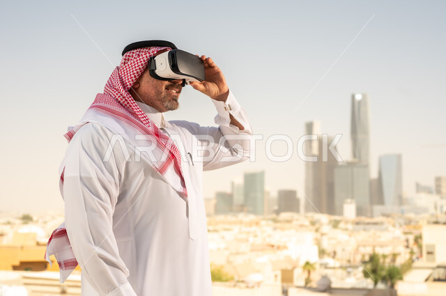  رؤية مستقبلية سعودية 2030، التفاعل مع الهندسة الافتراضية، رجل عربي خليجي سعودي يرتدي الثوب التقليدي والشماغ يضع نظارة الواقع الافتراضي يشاهد تطور المنشآت والمباني المعمارية في المدينة، نمو وتطور المجال الهندسي, استخدام أجهزة تقنية حديثة