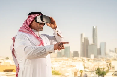  رؤية مستقبلية سعودية 2030، التفاعل مع الهندسة الافتراضية، رجل عربي خليجي سعودي يرتدي الثوب التقليدي والشماغ يضع نظارة الواقع الافتراضي يشاهد تطور المنشآت والمباني المعمارية في المدينة، نمو وتطور المجال الهندسي, استخدام أجهزة تقنية حديثة