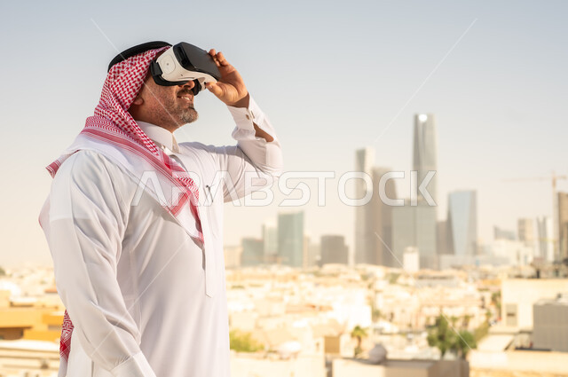 رؤية مستقبلية سعودية 2030، التفاعل مع الهندسة الافتراضية، رجل عربي خليجي سعودي يرتدي الثوب التقليدي والشماغ يضع نظارة الواقع الافتراضي يشاهد تطور المنشآت والمباني المعمارية في المدينة، نمو وتطور المجال الهندسي, استخدام أجهزة تقنية حديثة