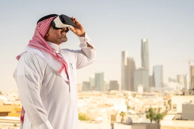  رؤية مستقبلية سعودية 2030، التفاعل مع الهندسة الافتراضية، رجل عربي خليجي سعودي يرتدي الثوب التقليدي والشماغ يضع نظارة الواقع الافتراضي يشاهد تطور المنشآت والمباني المعمارية في المدينة، نمو وتطور المجال الهندسي, استخدام أجهزة تقنية حديثة