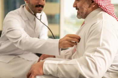 قياس  معدل ضربات القلب, مفهوم الطب والرعاية الصحية, المتابعة الدورية لفحص نبضات القلب, طبيب عربي خليجي سعودي يرتدي المعطف الطبي يقوم باستخدام سماعه الفحص الطبية لمريض كبير بالسن