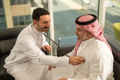  المتابعة الدورية لفحص نبضات القلب, طبيب عربي خليجي سعودي يرتدي المعطف الطبي يقوم باستخدام سماعه الفحص الطبية لمريض كبير بالسن, قياس  معدل ضربات القلب, مفهوم الطب والرعاية الصحية