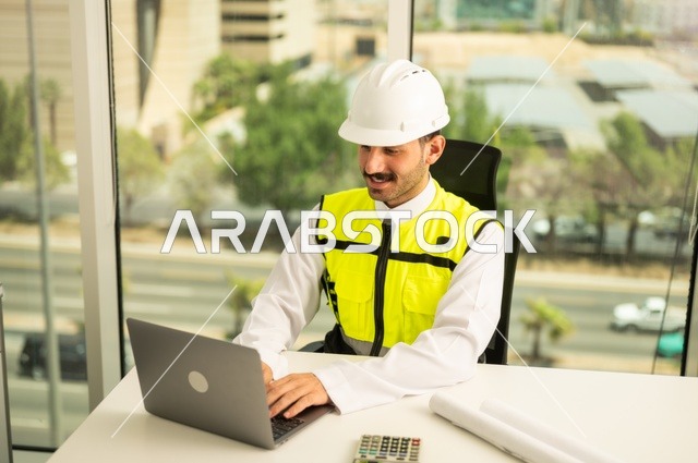 Integrating work with technology and tech, reviewing new engineering designs on a laptop, an Arab Saudi Gulf architect wearing work attire, supervising the implementation of architectural engineering projects and plans in construction.