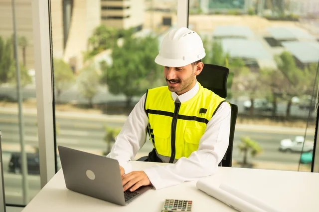Integrating work with technology and tech, reviewing new engineering designs on a laptop, an Arab Saudi Gulf architect wearing work attire, supervising the implementation of architectural engineering projects and plans in construction.
