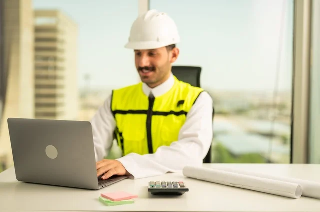 Integrating work with technology and tech, reviewing new engineering designs on a laptop, an Arab Saudi Gulf architect wearing work attire, supervising the implementation of architectural engineering projects and plans in construction.