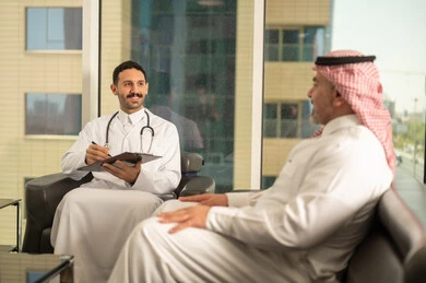  تدوين نتائج الفحوصات بالسجل الطبي لمريض كبير بالسن، حسن التعامل مع المراجعين، ايماءات البشاشة والسرور، طبيب عربي خليجي سعودي يرتدي الثوب التقليدي والمعطف الابيض يحمل بيده ملفات المرضى، العمل في القطاع الصحي, اعداد التقارير الطبية