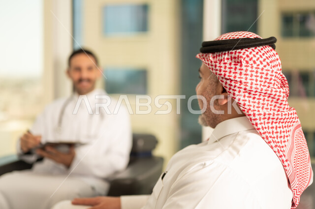  تدوين نتائج الفحوصات بالسجل الطبي لمريض كبير بالسن، حسن التعامل مع المراجعين، ايماءات البشاشة والسرور، طبيب عربي خليجي سعودي يرتدي الثوب التقليدي والمعطف الابيض يحمل بيده ملفات المرضى، العمل في القطاع الصحي, اعداد التقارير الطبية